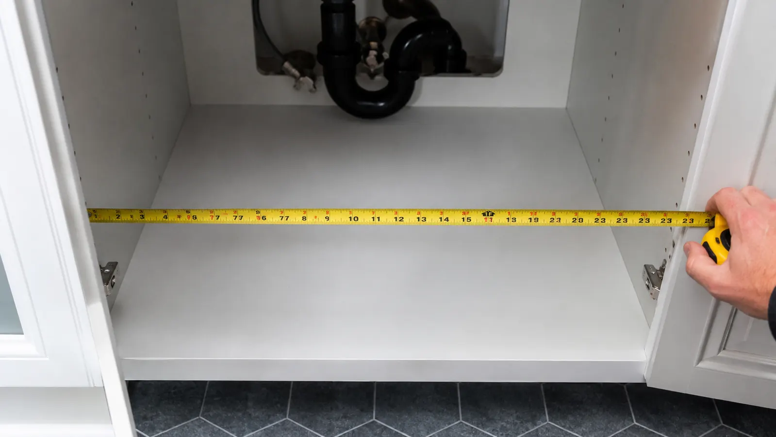 Measuring tape stretched across the interior width of an empty bathroom cabinet under the sink showing 22 inches