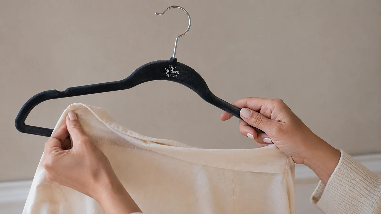 Close-up of a hand pulling a blouse off a slim velvet hanger, shoulder groove visible, clothes not slipping
